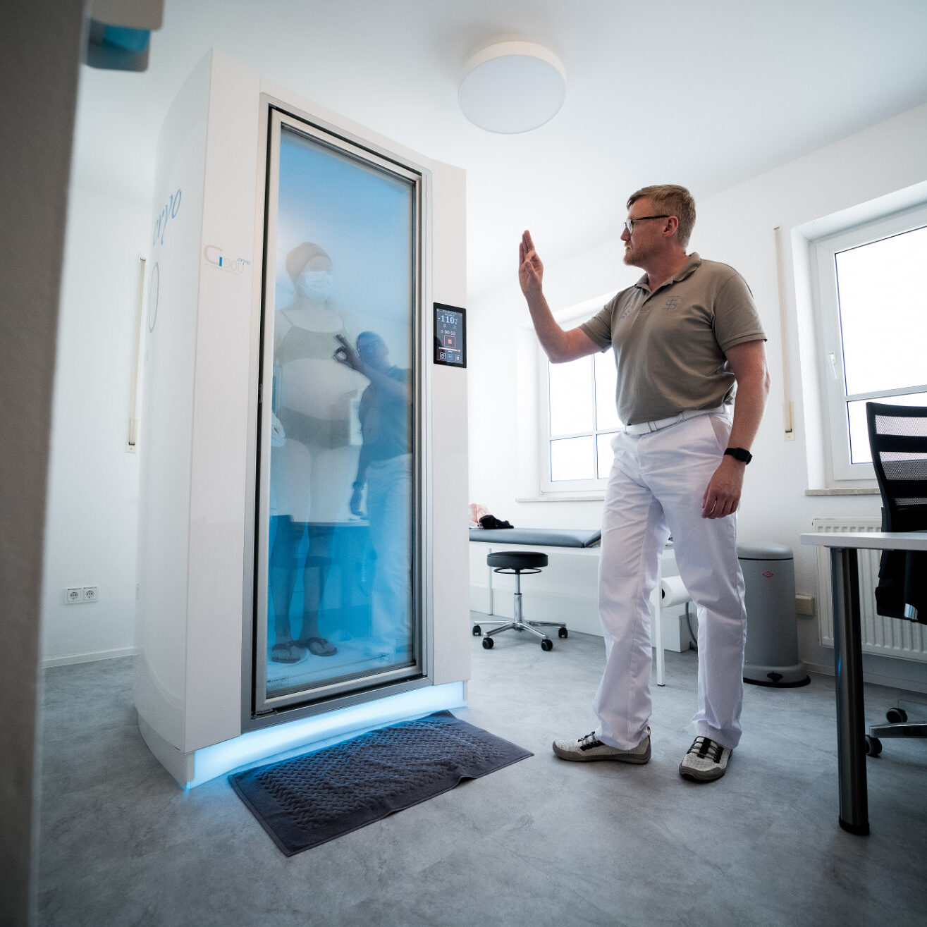 Dr. Thorsten Schmidt gibt OK-Zeichen an eine in der Kältekammer stehenden Patientin